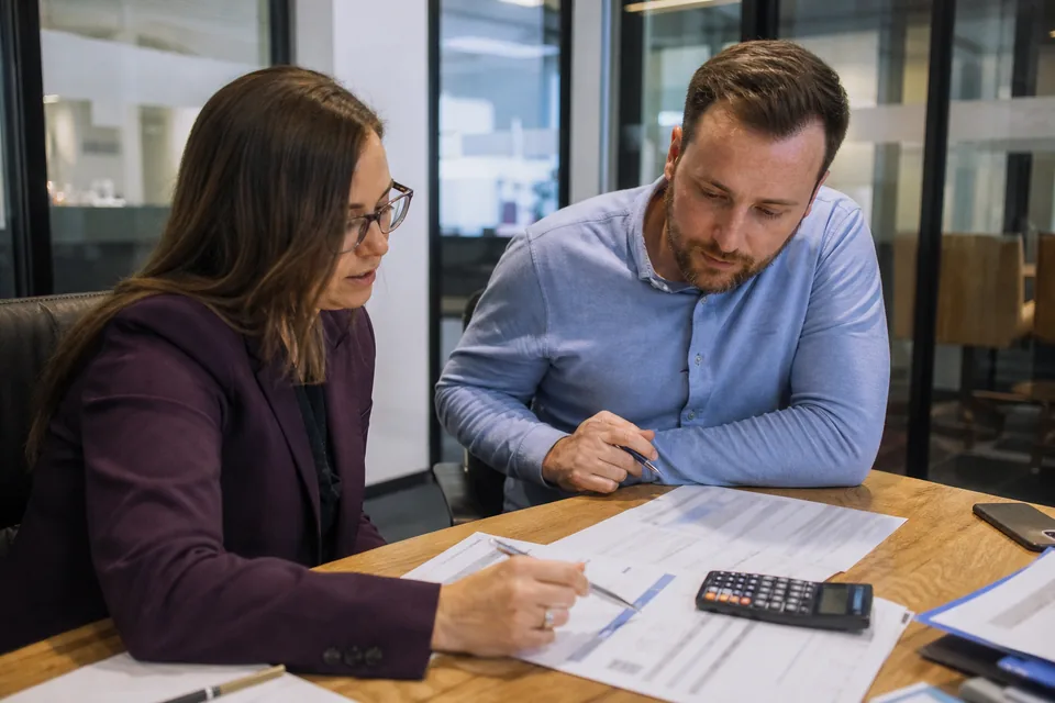 Finance manager and project office lead comparing software invoices with a calculator at a meeting table