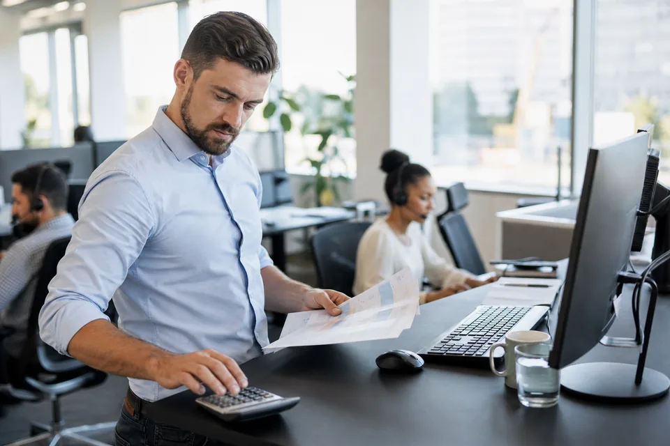 Sales team leader comparing per-seat software costs on a printed spreadsheet in an open-plan office