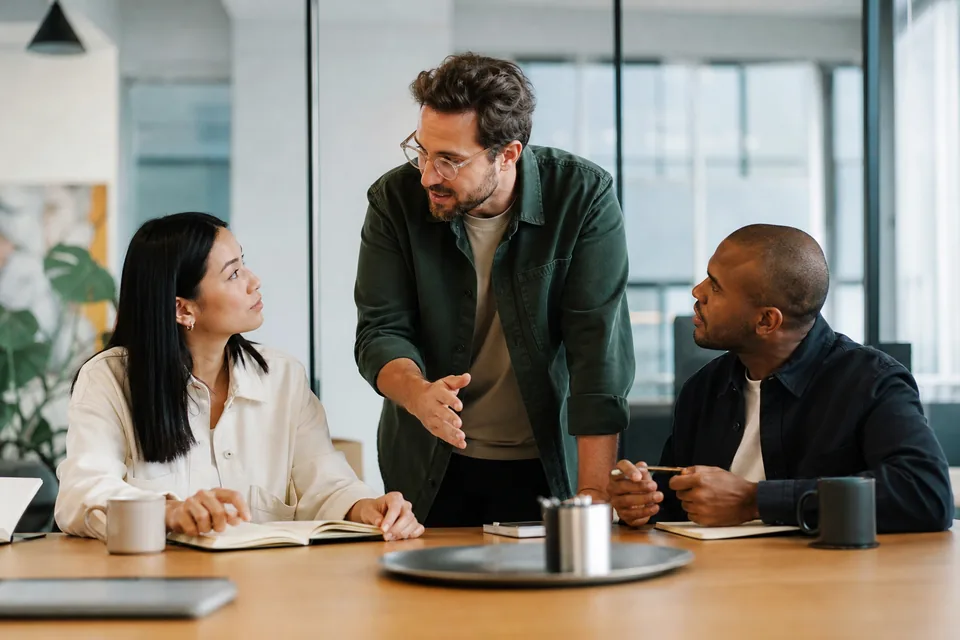 Operations team lead handing out new work to two teammates at their desks